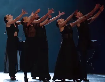 Un grupo de bailarines danzan y tienen alzadas sus manos 