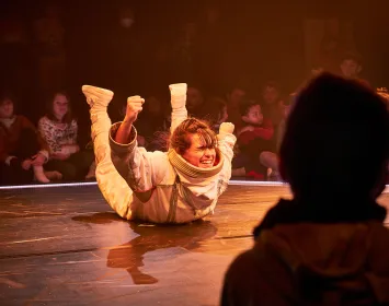 Una bailarina con un traje de astronauta esta sobre el suelo con las manos y pies levantados. 