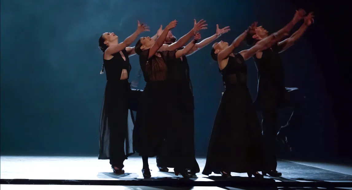 Un grupo de bailarines danzan y tienen alzadas sus manos