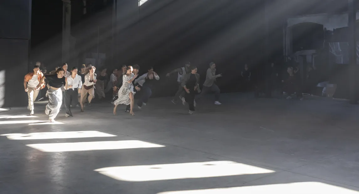Un grupo de bailarines corren. Rayos de luz entran por las ventanas.