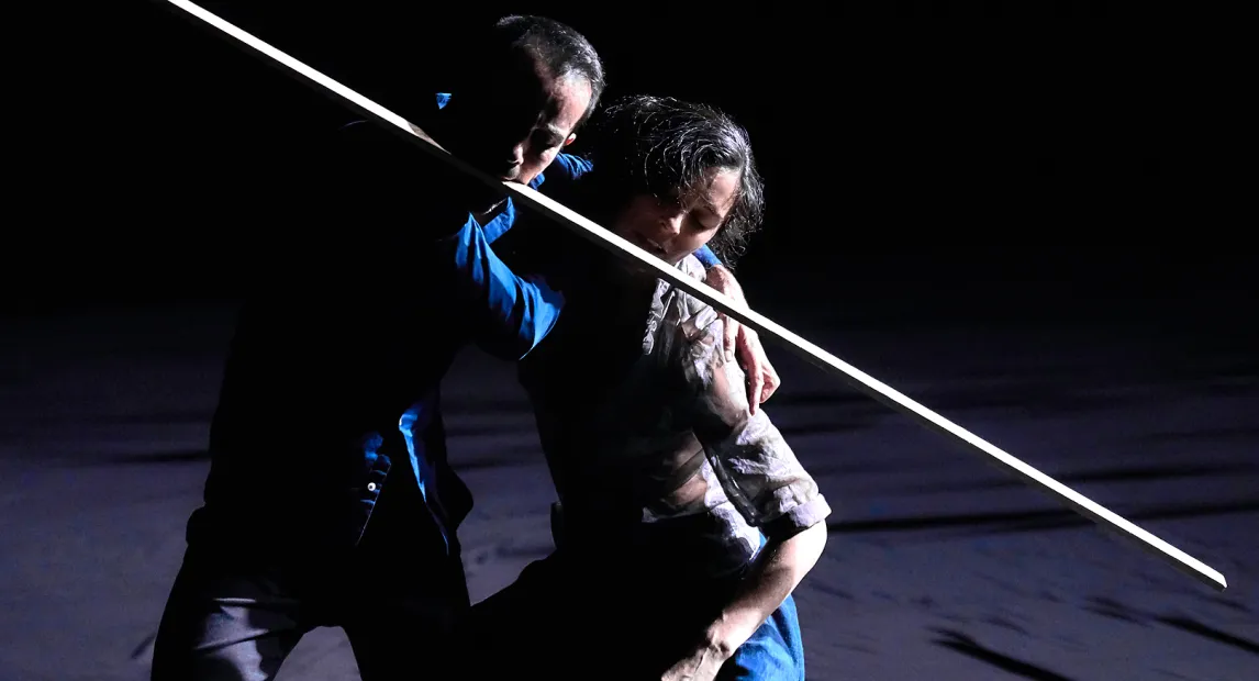 Una pareja de bailarines sostienen un listón de madera con su boca.