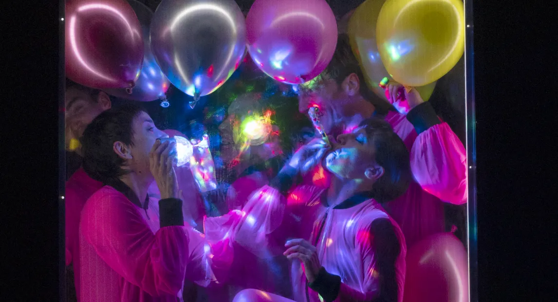 Two dancers perform inside a frame filled with colorful balloons.