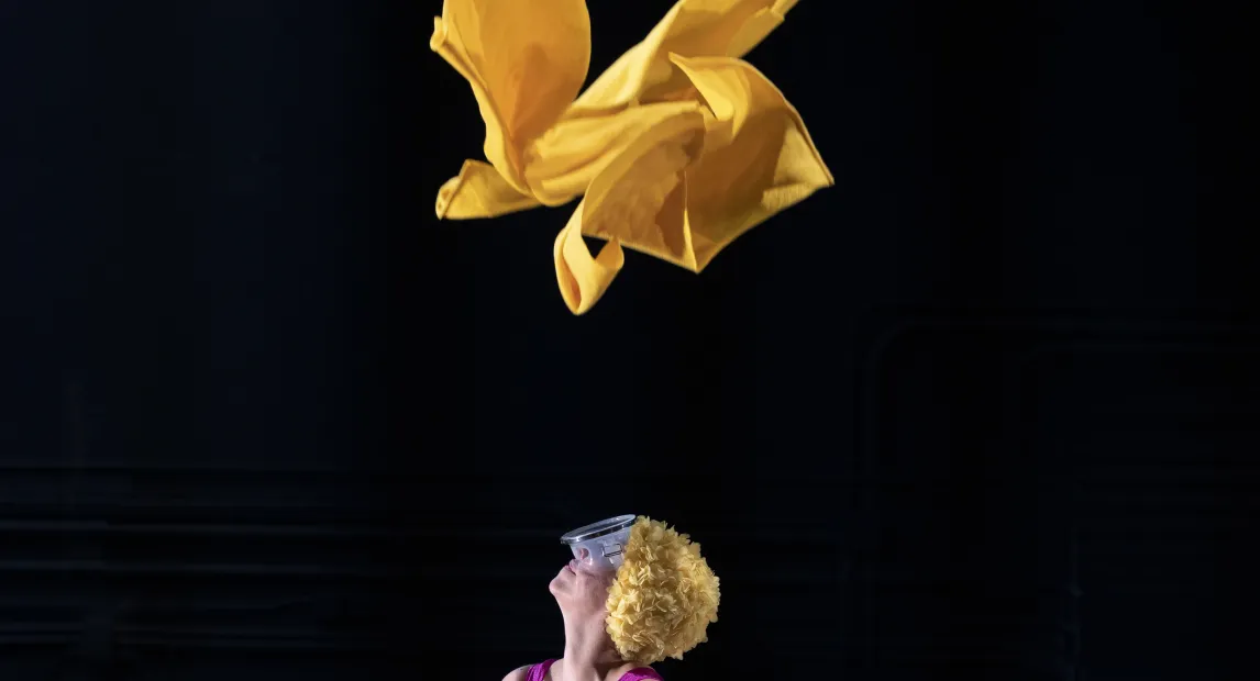 A woman watches and waits for a piece of yellow fabric to fall to the ground.