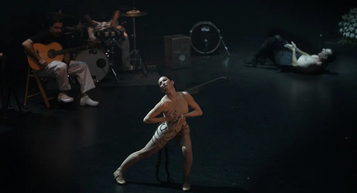 A ballerina on stage looks upward, illuminated by a dim light