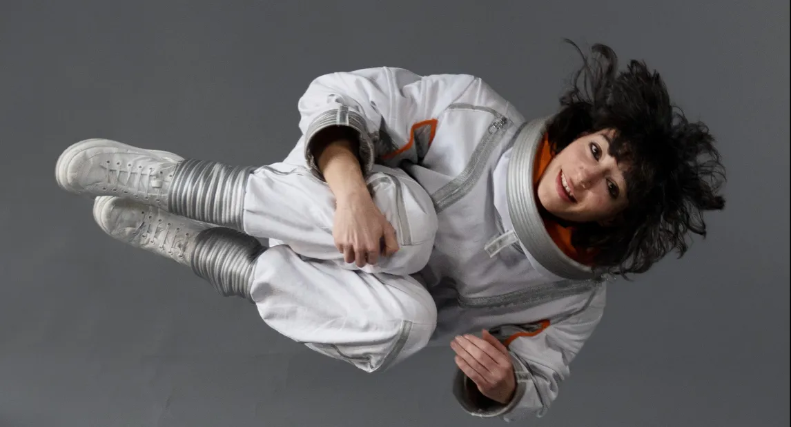 Una bailarina con traje de astronauta esta sostenida en el aire, como flotando