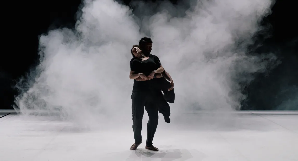 Dos bailarines danzan, hay humo en el escenario.