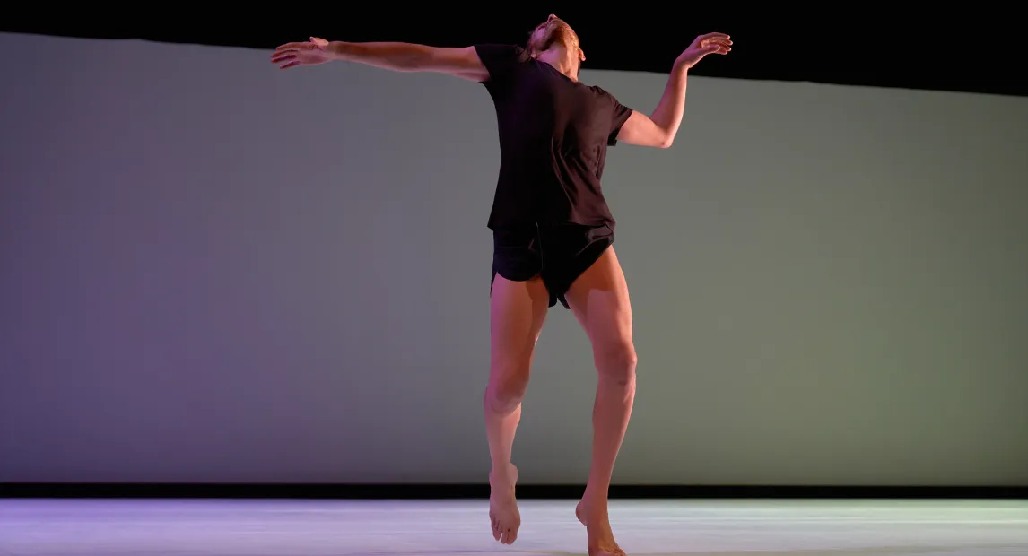 Un bailarín danza, tiene su brazos alzados.