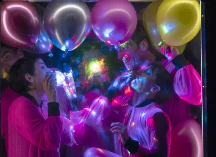 Two dancers perform inside a frame filled with colorful balloons.