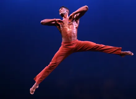 Un bailarín está sostenido en el aire. tiene un pantalón rojo. Sus pies se estiran en el aire.