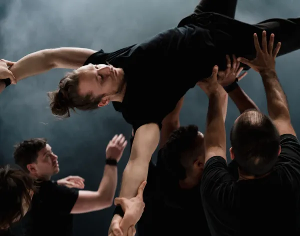 Un grupo de bailarines sostienen con sus manos en el aire a otro.