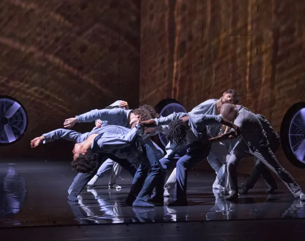 Un grupo de bailarines son iluminados por una luz desde arriba.