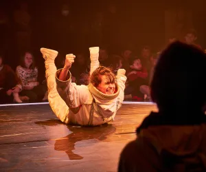 Tristán Pérez Martín Una bailarina con un traje de astronauta esta sobre el suelo con las manos y pies levantados.