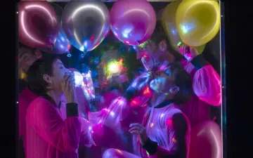 Two dancers perform inside a frame filled with colorful balloons.