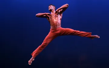 Un bailarín está sostenido en el aire. tiene un pantalón rojo. Sus pies se estiran en el aire. 